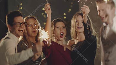 Guys celebrating by waving fireworks, enjoying party on New Years or Christmas Eve. Close up portrait friends holding