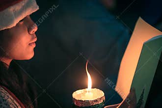 Young Child Reading Book Beside Warm Candle Light In Quiet Night