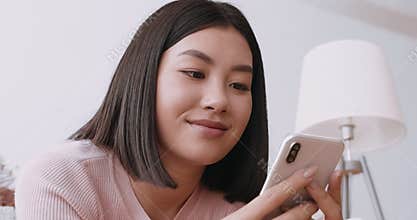 Close up portrait of cheerful asian woman texting on cellphone, chatting with friends at home