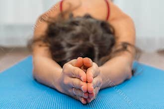 A brunette woman is engaged in fitness, yoga classes. She is dressed in a black top and red leggings, bent over her leg