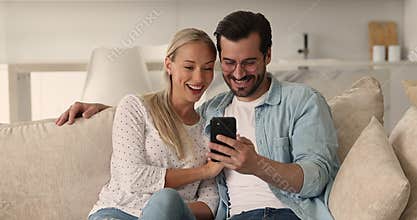 Millennial couple resting on sofa having fun using smartphone app