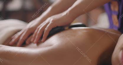 Beautiful young brunette woman gets hot stones massage at day spa. Attractive female relaxing at spa center with a stone