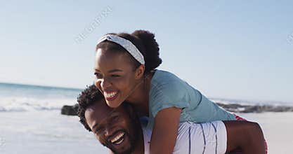 African american man smiling and carrying african american woman piggyback on the beach