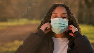 African American girl biracial teenager young woman outside taking off a face mask during COVID-19 Coronavirus pandemic