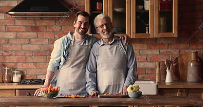 Happy bonding two male generations in aprons looking at camera.