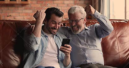 Overjoyed young man celebrating online success with older father.