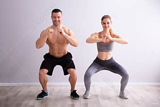 Fitness Couple In Sportswear Doing Squat Exercises At Gym