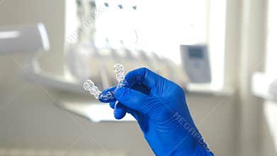 Modern transparent aligners or braces to straighten teeth in cosmetic dentistry and orthodontics. Female hand in blue