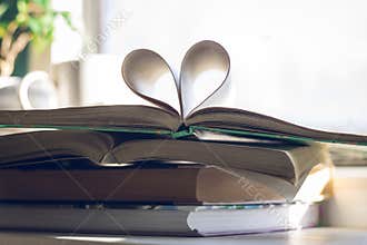 Stack of books with open one at the top. Heart of pages on background of open window. Love to read concept