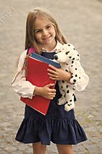 Adding fun to study. Happy child hold toy dog and books outdoors. Back to school supplies. Fashion uniform. Formal dress