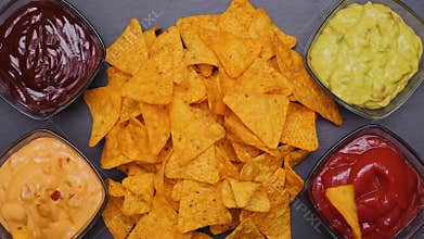 Hands taking tortilla chips dipping them in various flavoured sauces