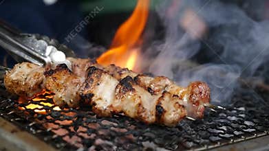 Handheld, slow motion close up of smoky pork belly skewers on a fiery charcoal hibachi grill