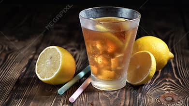 Glass of iced tea with ice cubes and sliced lemons on rustic wooden table or background. Healthy refreshing lemonade for