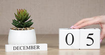 Wooden calendar with an important event for December 5, a woman`s hand sets the date on the calendar. Winter season.