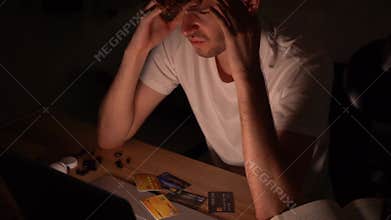 White man with credit card debt sitting in front of his laptop computer trying to solve the problem with stress at night alone.