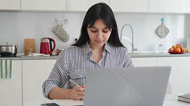 Young indian latin mixed race girl sitting at desk with pc at kitchen table.
