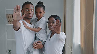 African family black serious young afro parents with little daughter standing indoor holding their palms in front of