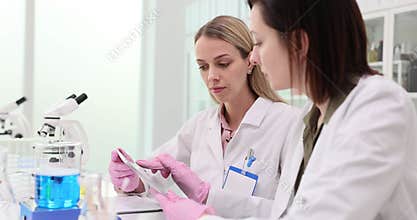 Two scientists collaborate in a modern laboratory during the day and work on a tablet