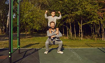 Child boy sitting on fathers shoulders doing sport fit exercises together on gymnastic bar.