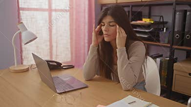 A beautiful brunette hispanic woman appears stressed at her laptop in a home office setting, capturing a moment of work-related