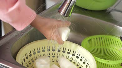 Woman preparing meals in kitchen, cleaning washing cassava, preparation for cooking