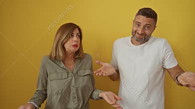 Couple shrugging in confusion over isolated yellow background with man and woman looking puzzled and amused