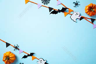 Halloween flat lay composition with party decor, bunting flag garland, pumpkins, ghosts, spiders, and bats on a blue background