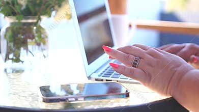 A woman is typing on a laptop while holding a cup of coffee. The laptop is open to a website and the woman is using her