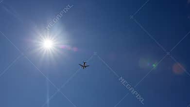 Airplane is flying under the sun in a clear blue sky
