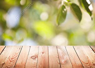 Empty wooden table with foliage bokeh background.