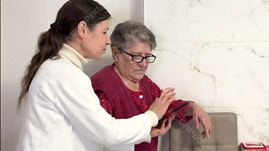 A middle-aged women explains the settings on a cell phone to an elderly grandmother.