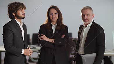 A businesswoman in glasses and a business suit stands in the office with her partners. A team of businessmen posing