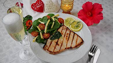 Grilled swordfish steak with fresh salad, tomatoes and cheese on a plate rotating. Valentines day. Pour champagne into a glass.