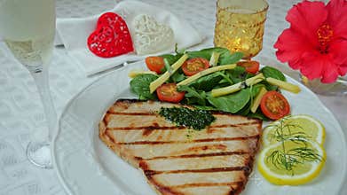 Grilled swordfish steak with fresh salad, tomatoes and cheese on a plate rotating. Valentines day. Pour champagne into a glass.