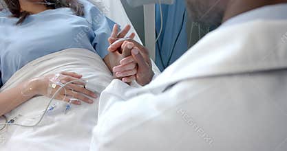 Diverse male doctor holding hand of female patient with oximeter in hospital bed, slow motion
