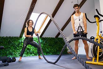 Smiling sportswoman doing exercise with battle ropes in fitness club