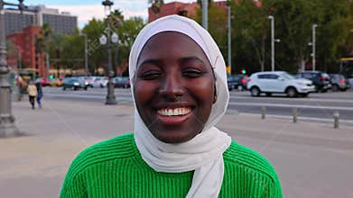 Portrait of young black muslim woman wearing hijab smiling at camera outdoors