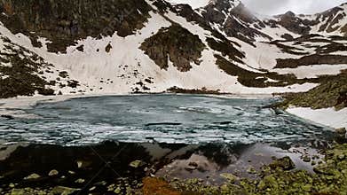 adventure, couple standing on a rocky hill overlooking a stunning snow-capped mountain and lake, aerial view, flying