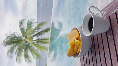 morning cup of coffee and sliced mango on the table by the swimming pool with an incredible sea view of the sea and palm