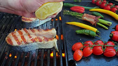Salmon fish steak on grill with vegetables. Chef hand squeezes lemon on fish steak grilled. Slow motion. Close up