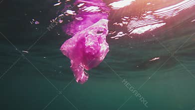 Plastic pollution, red purple plastic bag in blue water. Slow motion, discarded plastic bag drifts slowly under the