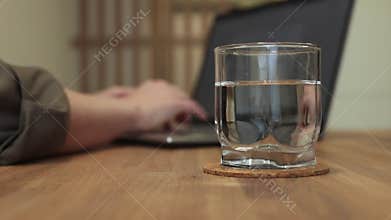 Water glass, pure aqua cup on work desk in home office for healthy business life, blurred hands