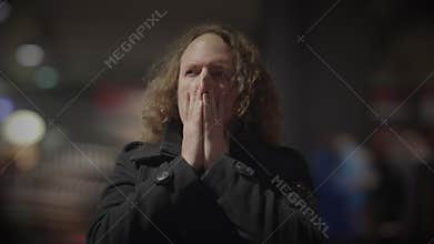 Man with long curly hair covering mouth in contemplation by window