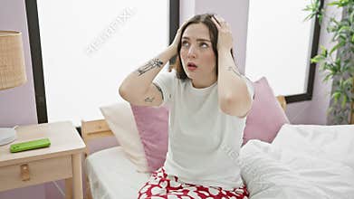 Stressed young woman in pyjama sits on bed aching from painful migraine. hands on head, wearing stress of intense headache pain,