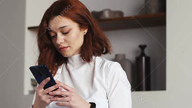 Happy caucasian girl holding cell phone using smartphone device at home. Smiling young woman blogger subscribing new