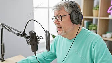 Mature man with headphones speaks into microphone in radio studio, conveying podcasting or broadcasting professionalism