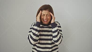 Hispanic woman in striped sweater, aching from severe headache. stressed and in pain, hands over head. isolated over white