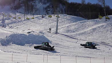 Two snow groomers assemble heap of snow on slope