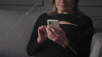 A woman is using a smartphone while sitting on a grey couch in a modern home interior