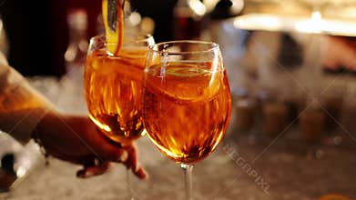 Bartender makes two glasses of cocktail Aperol spritz on bar counter, adds fresh orange slices. Typical alcoholic